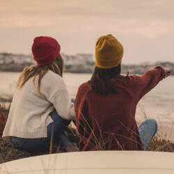 Kaksi nuorta naista istuu rantakivillä.