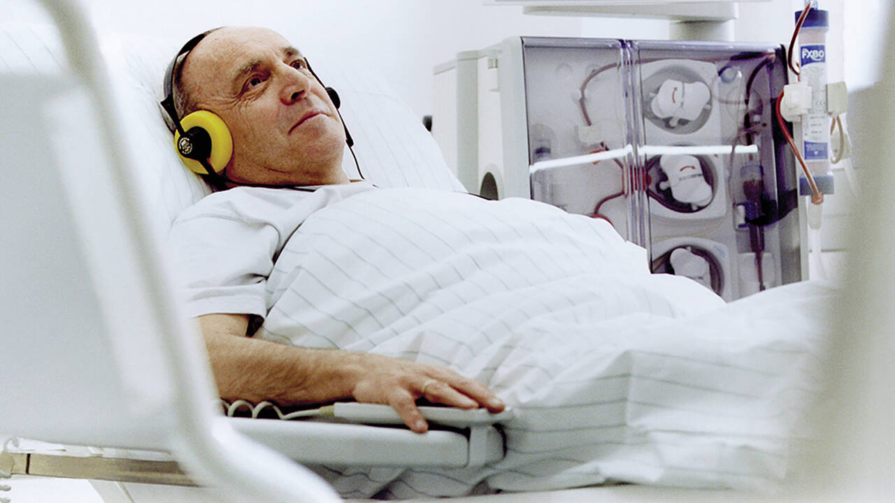 Mies makaa sängyssä kiinnitettynä hemodialyysilaitteeseen.