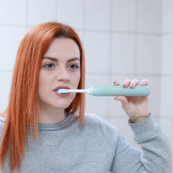 Nuori nainen harjaa hampaita sähköhammasharjalla.